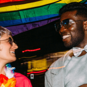 One person of colour and one white person waving the pride flag at night