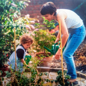 A white mother and child in a garden, tending flowers in sunshine. The picture is taken on old-style film, denoting that it's an old photo