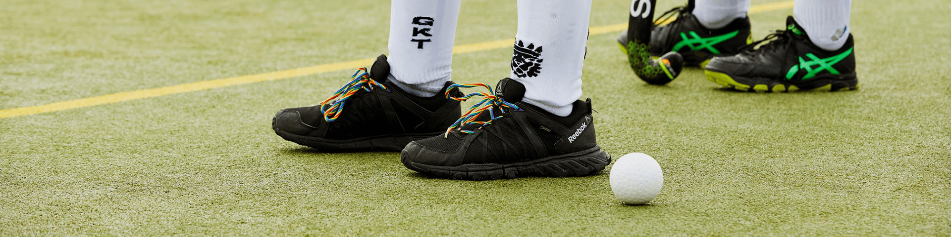 Sports person wears Rainbow Laces in black boots on a playing field